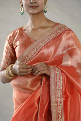 Woman wearing an orange saree with intricate patterns on a neutral background.