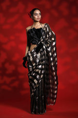 A woman wearing a black and silver party wear saree against a red background representing the Best Saree look for parties and weddings
