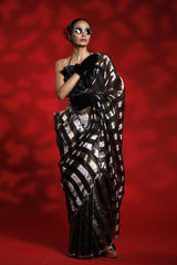 A woman wearing a black and silver party wear saree against a red background representing the Best Saree look for parties and weddings