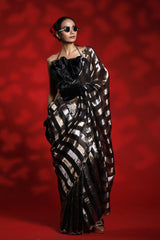 A woman wearing a black and silver party wear saree against a red background representing the Best Saree look for parties and weddings
