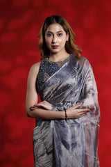 A woman wearing a shiny silver party wear saree with a red background