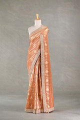 Peach tissue silk saree with intricate patterns and embellished border draped on a mannequin against a plain background