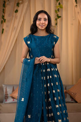 A woman in a blue traditional frock suit with a matching dupatta, standing in a decorated indoor setting.