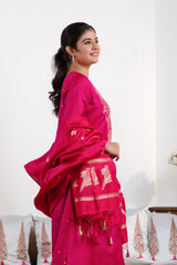 A woman in a traditional pink salwar suit and pink banarasi dupatta is standing in a decorated room.