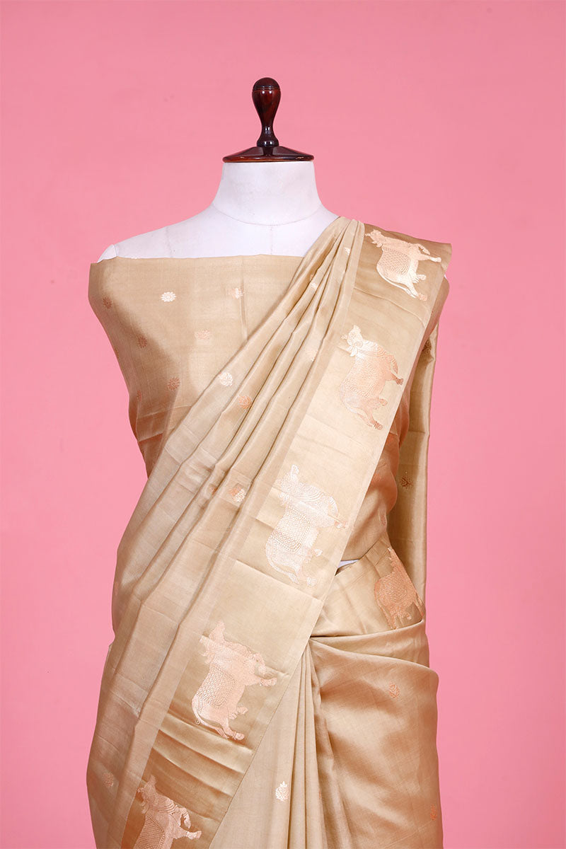A beige Banarasi silk saree with gold zari border for Navratri, Diwali, Durga Puja, and weddings, displayed on a mannequin. 
