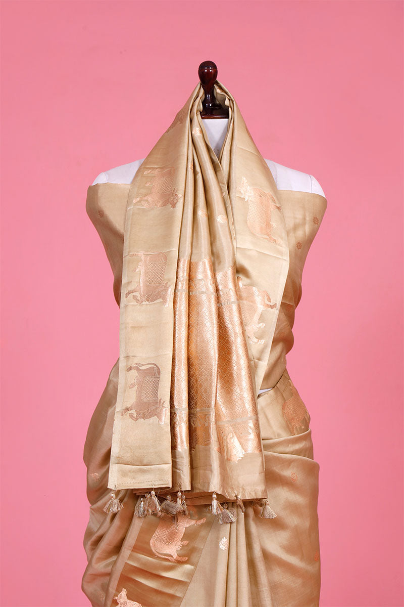 A beige Banarasi silk saree with gold zari border for Navratri, Diwali, Durga Puja, and weddings, displayed on a mannequin. 