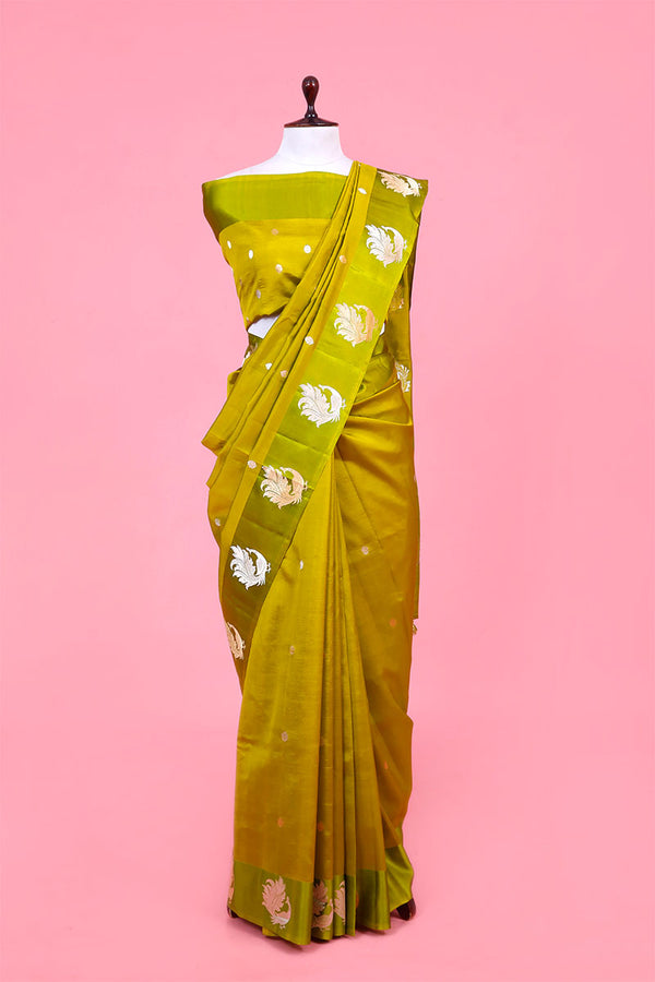 A lime green Banarasi silk saree with gold and silver zari kadhwa woven peacock motifs displayed on a mannequin against a pink background.