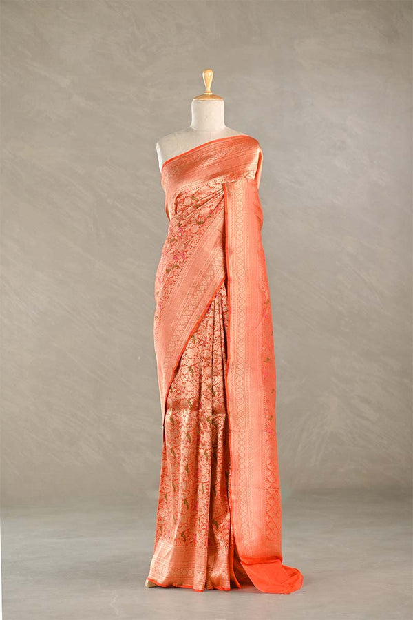 Coral saree with intricate patterns on a mannequin against a neutral background