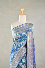 Teal blue Banaarsi silk saree with floral and meenakari zari work draped on a mannequin against a gray background