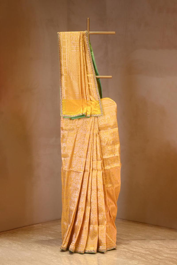 Yellow saree with green border on a wooden stand against a brown background