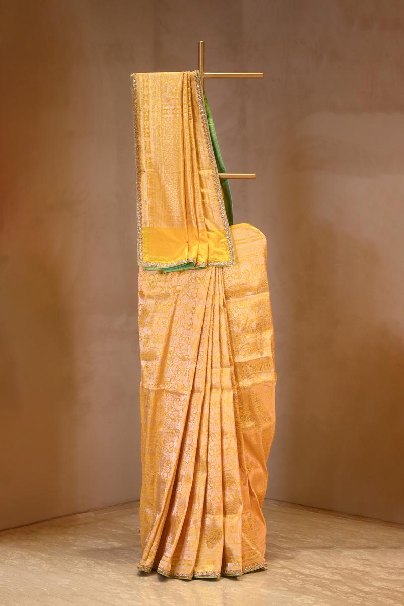 Yellow saree with green border on a wooden stand against a brown background