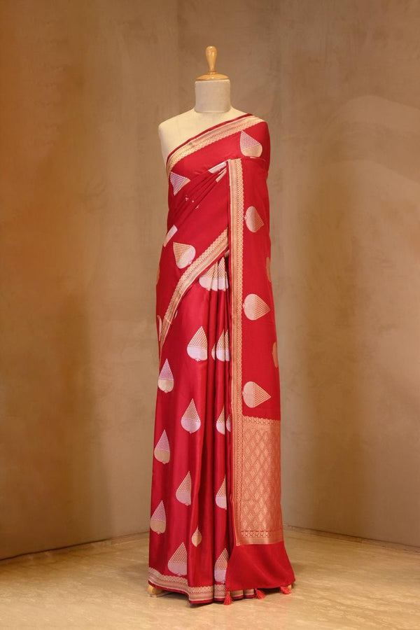 A red Banarasi silk saree with silver-gold zari motifs on dummy