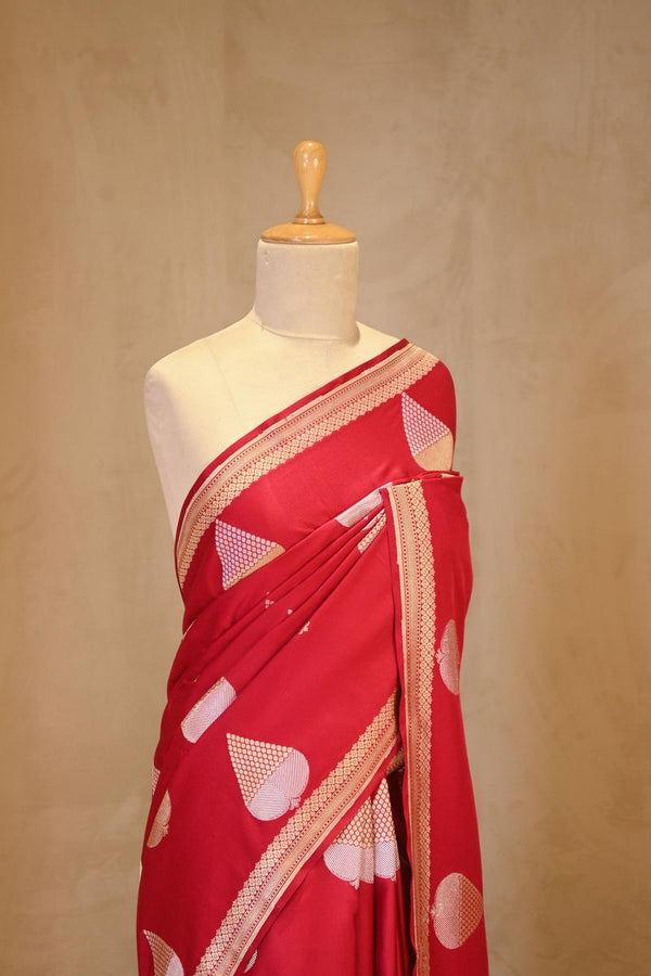 A red Banarasi silk saree with silver-gold zari motifs on dummy