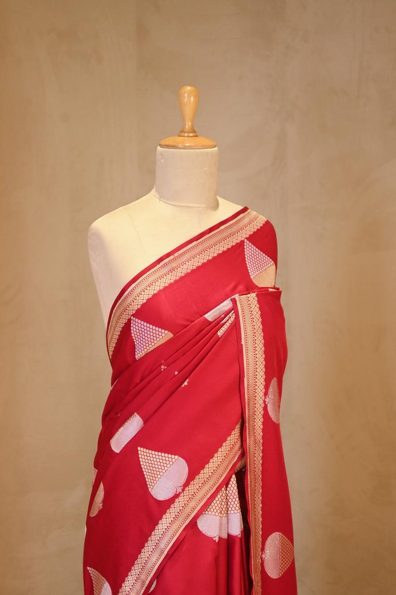 A red Banarasi silk saree with silver-gold zari motifs on dummy