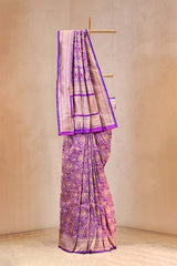Purple and pink saree with a matching blouse on a wooden stand against a beige background