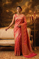 Woman in a pink RANGKAT BANARASI saree standing in an elegant room with a candelabrum and sofa.