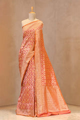 Close up of Coral Peach Banarasi Katan Silk Saree showing gold zari woven brocade geometrical floral jaal and resham butas on the body with a contrasting gold zari border.