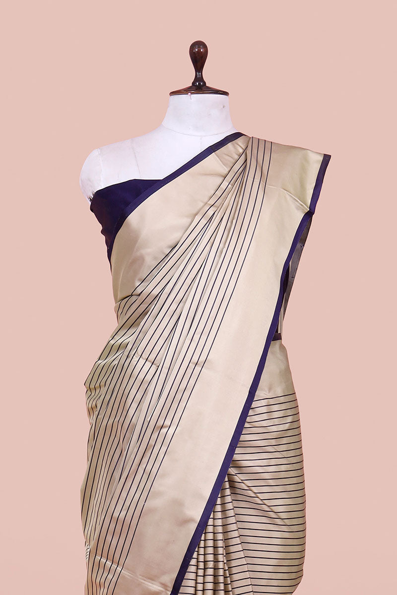 Beige saree with blue border on a mannequin against a beige background