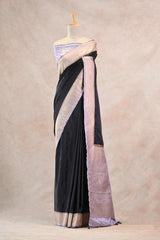 Mannequin draped in Black Saree with gold zari against a beige background. 