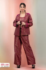 Woman wearing a maroon traditional outfit with a matching jacket and pants on a gradient background.