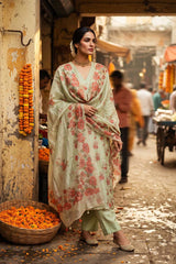 A woman stands wearing a light sage green traditional outfit with a coral floral print and matching dupatta.