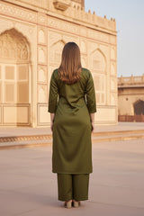 A woman in a green silk salwar suit set outfit standing in front of an architectural structure.