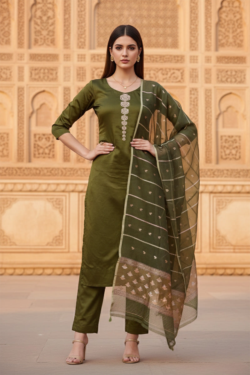 A woman in a green silk salwar suit set outfit standing in front of an architectural structure.