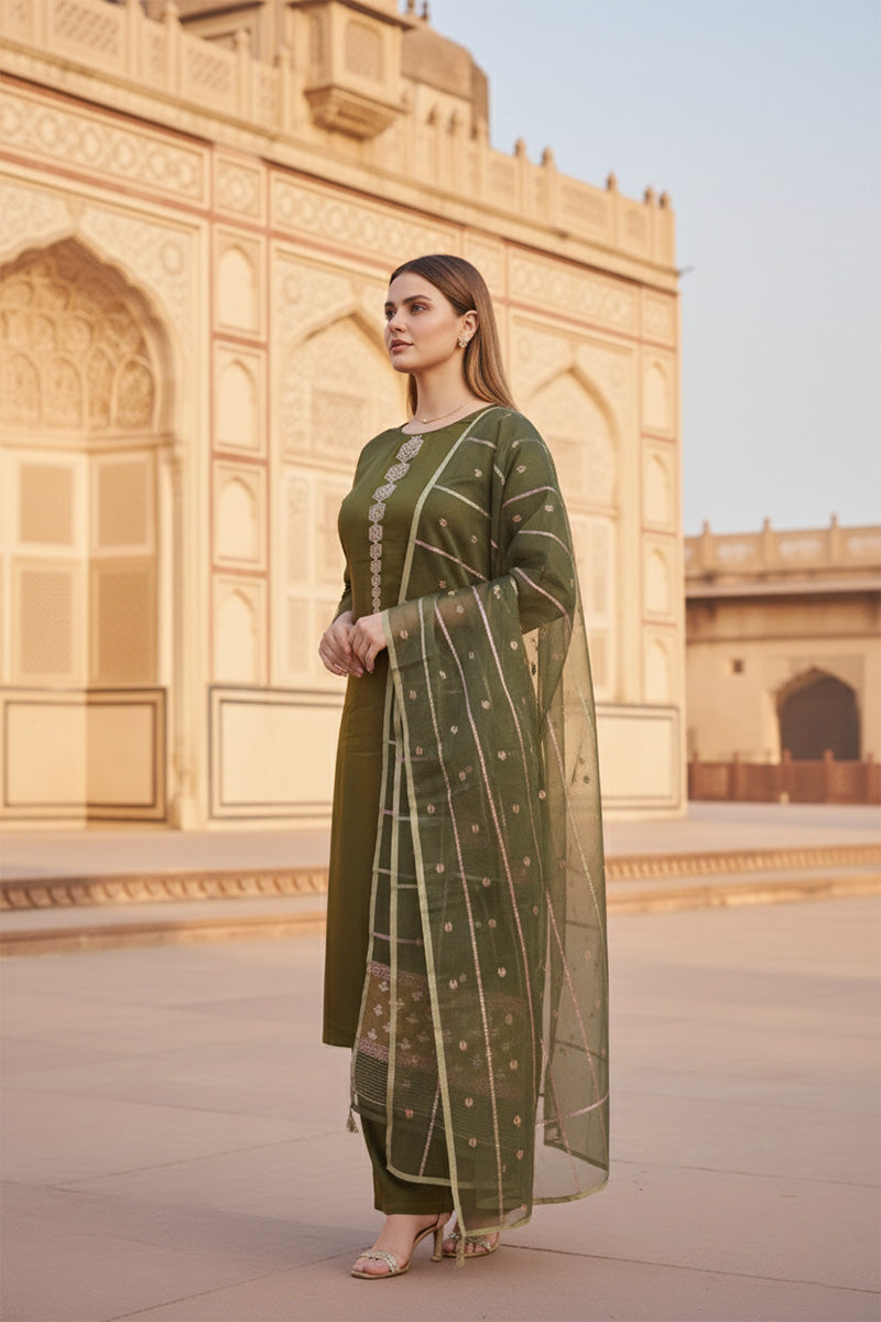 A woman in a green silk salwar suit set outfit standing in front of an architectural structure.