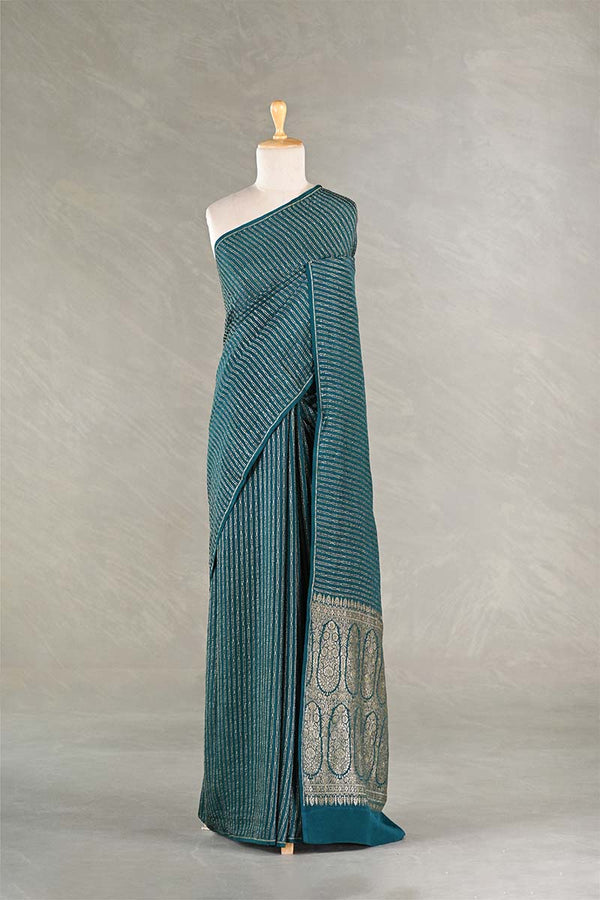 Teal saree with a patterned border on a mannequin against a plain background