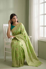 Woman wearing a light green saree sitting on a white chair in a room with a window.