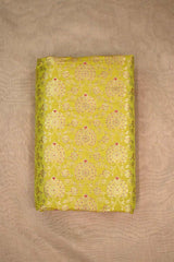 A lime green silk fabric with gold zari woven floral pattern with red accents on a beige background