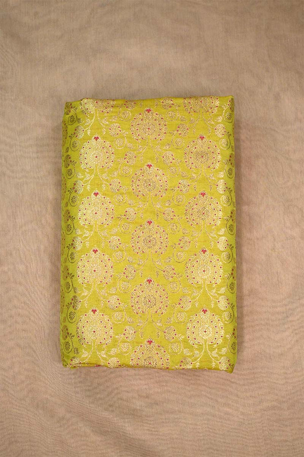 A lime green silk fabric with gold zari woven floral pattern with red accents on a beige background