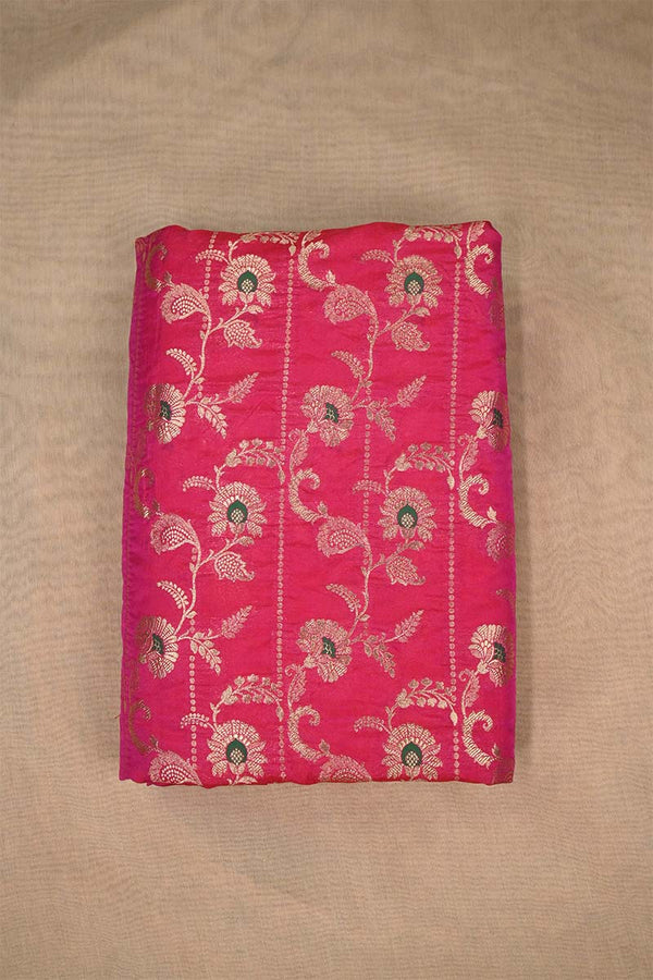 Close-up of pink Banarasi silk fabric with gold floral embroidery woven and green accents on beige background