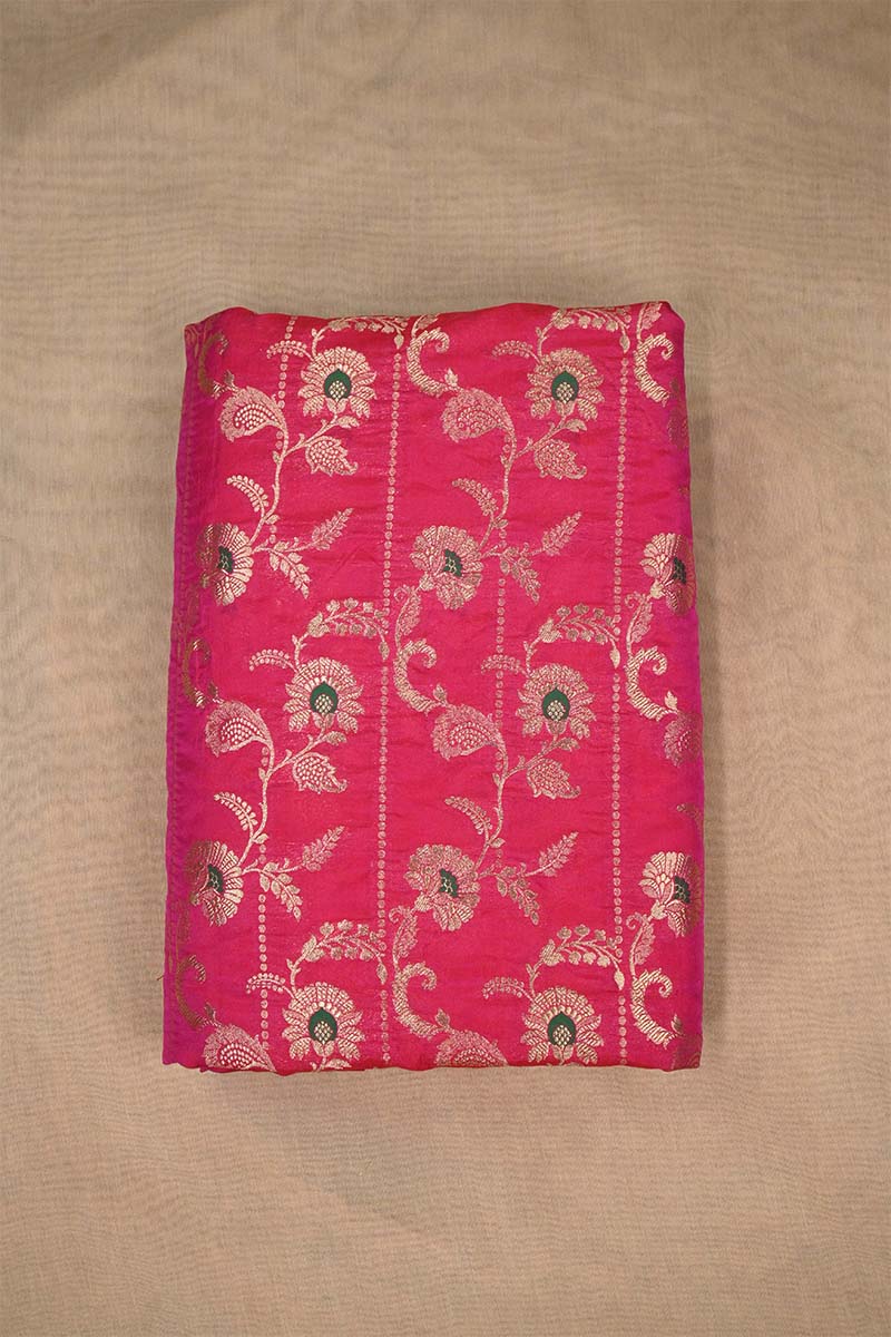 Close-up of pink Banarasi silk fabric with gold floral embroidery woven and green accents on beige background
