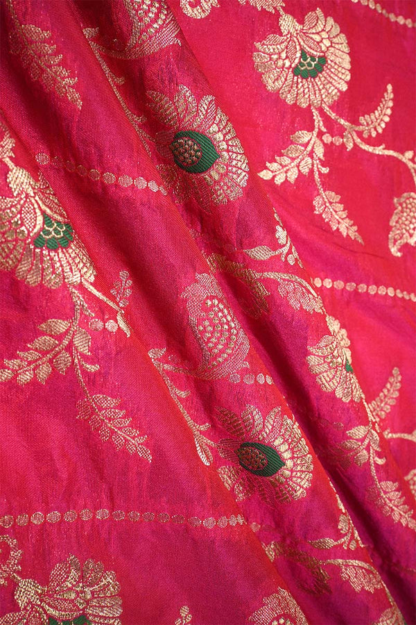 Close-up of pink Banarasi silk fabric with gold floral embroidery woven and green accents