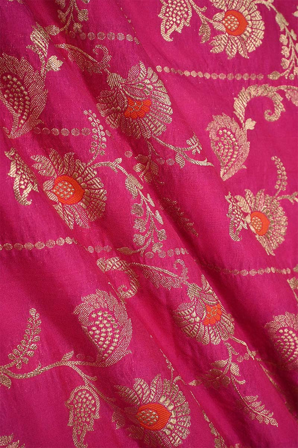 Close-up of pink Banarasi silk fabric with gold floral embroidery woven and green accents