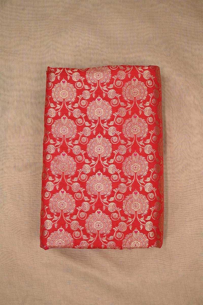 Close-up of red Banarasi silk fabric with intricate gold floral pattern on beige background
