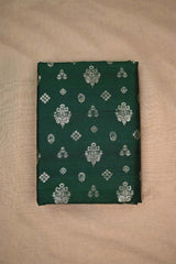 Close-up of bottle green raw silk fabric with gold and green floral patterns on beige background
