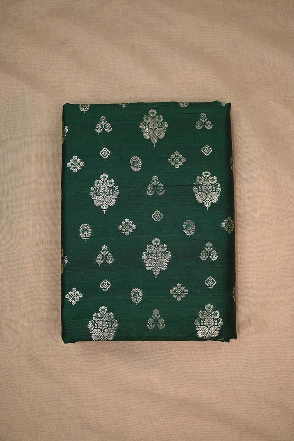 Close-up of bottle green raw silk fabric with gold and green floral patterns on beige background