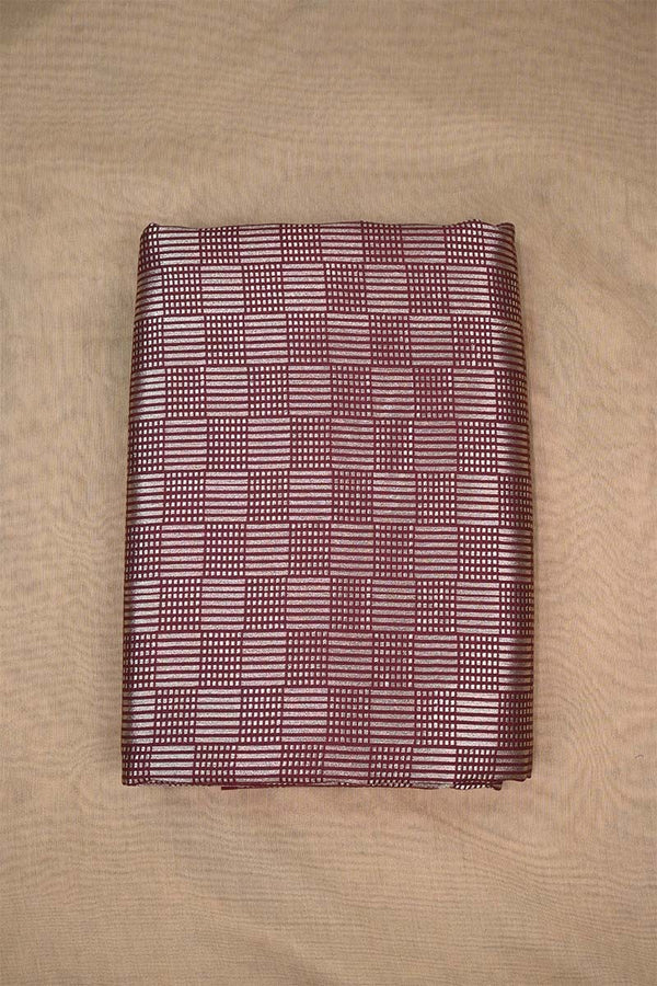 Close-up of a maroon Banarasi silk fabric with a subtle geometric pattern on beige background