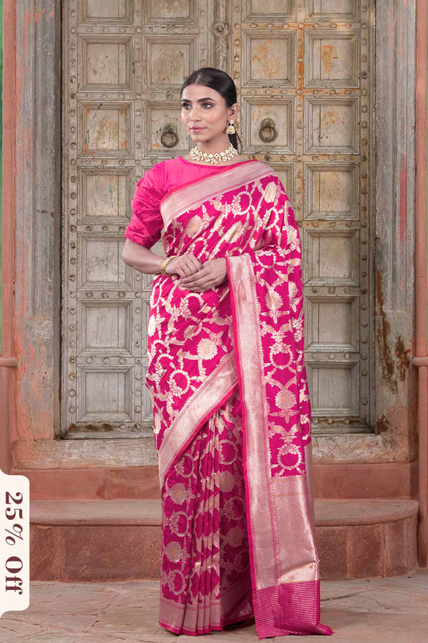 Woman wearing a pink saree with a pattern in front of an ornate door.