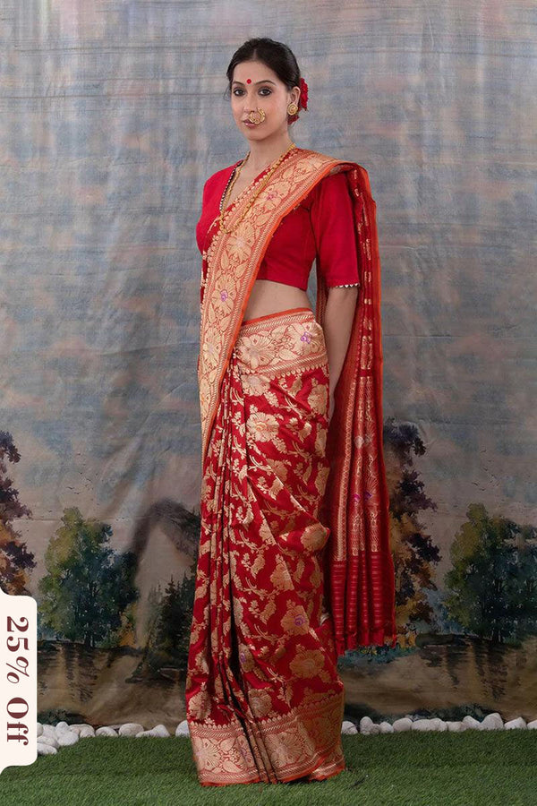 Woman wearing a red saree with gold patterns against a scenic backdrop