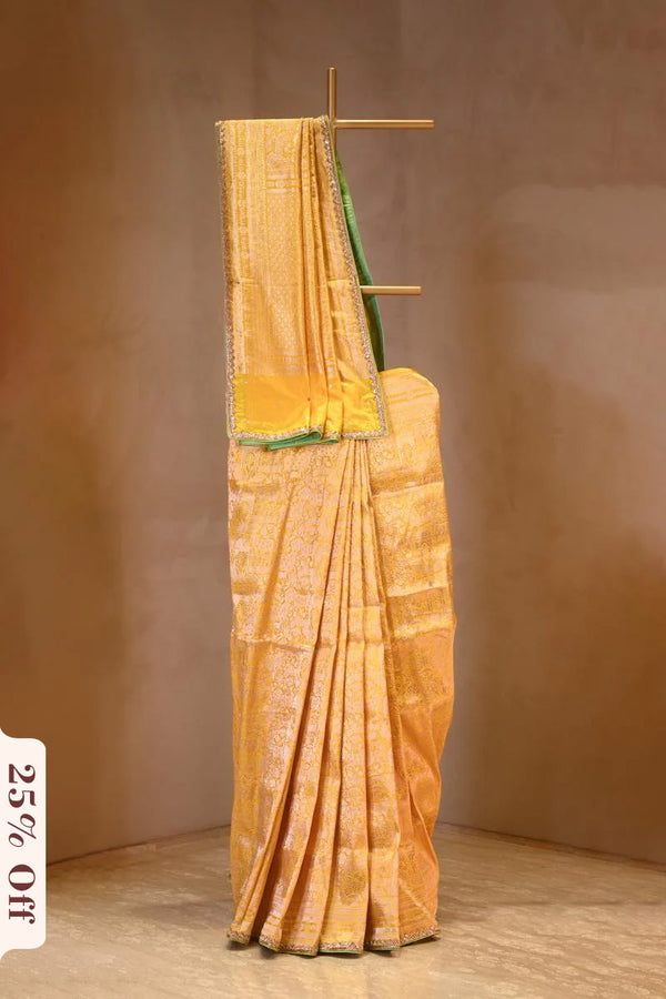 Yellow saree with green border on a wooden stand against a brown background