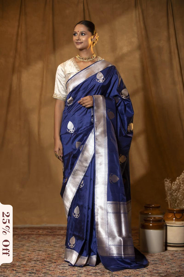 Woman wearing a blue saree with silver border against a brown curtain background