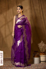 Woman wearing a purple saree with gold details against a brown background