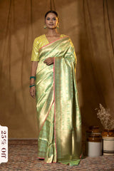 Woman wearing a green saree with a gold border against a brown background