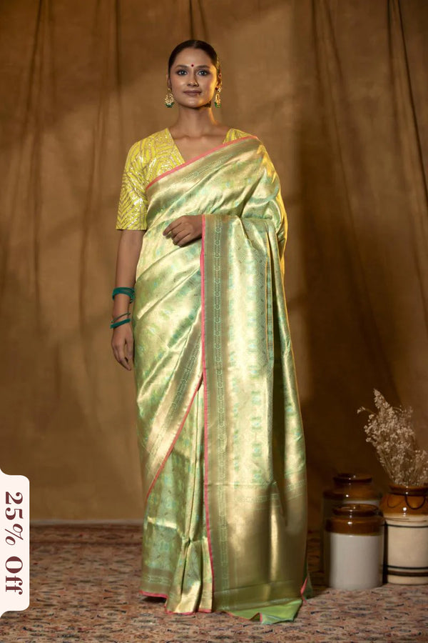 Woman wearing a green saree with a gold border against a brown background