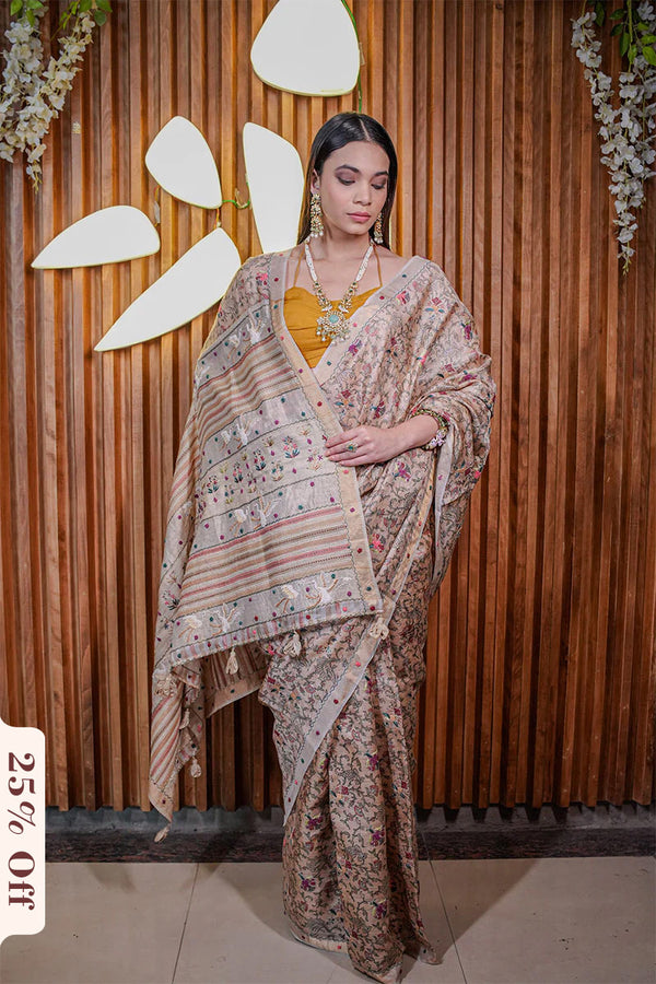 Woman in a floral saree standing against a wooden wall with decorative elements.