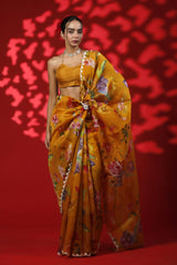 A woman wearing a mustard yellow party wear saree with floral prints against a red background