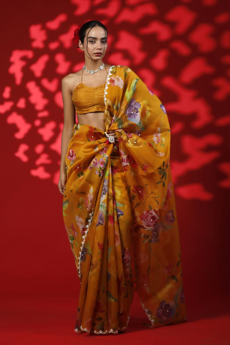 A woman wearing a mustard yellow party wear saree with floral prints against a red background